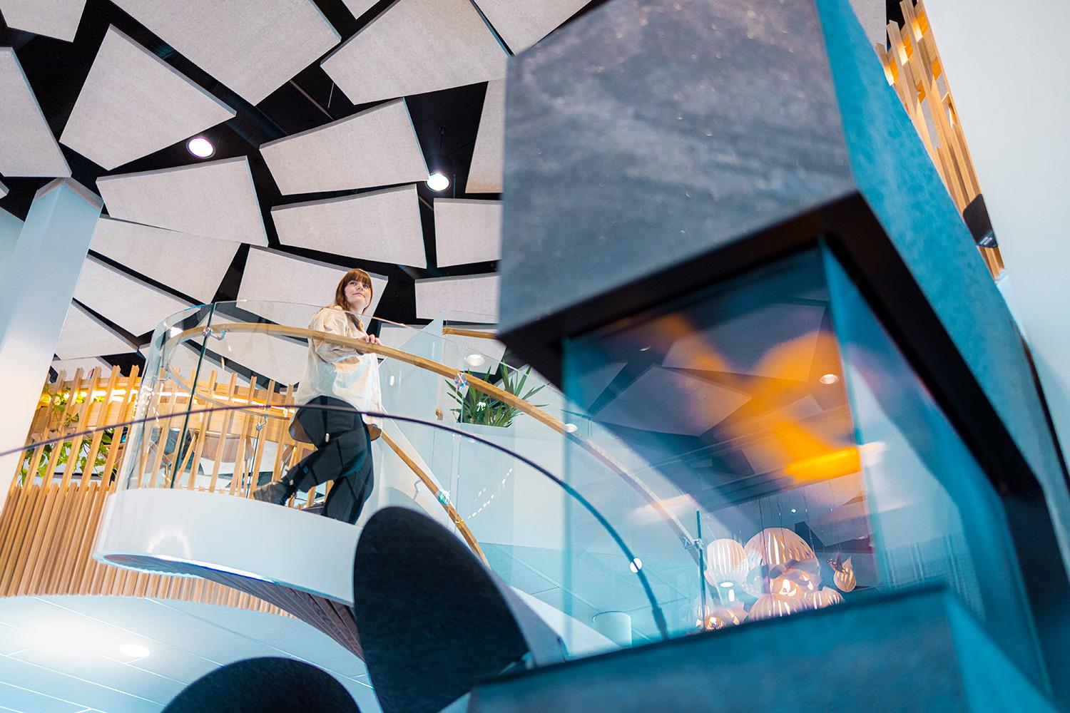 Savilahden uusi ja moderni CoWork-tila, jossa nainen laskeutuu kaarevia portaita alakertaan. Paljon lasia, puuta ja valoja.
