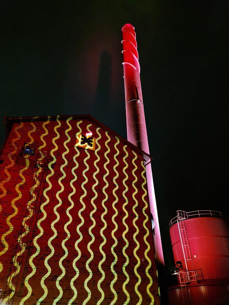 Lämpökeskuksen punaiseen seinään on heijastettu keltaisia aaltoja.