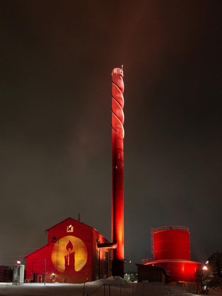 Lämpövoimalaitos ja sen korkealle kohoava piippu loistavat punaisina pimenevässä syysillassa.
