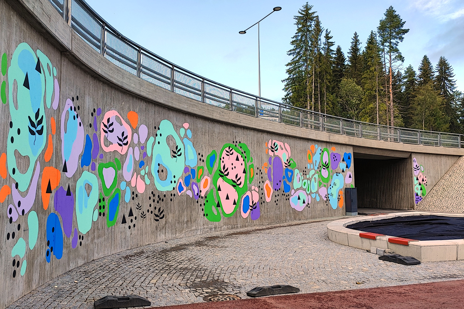 Sillan kupeessa oleva muraali, joka koostuu abstrakteista värikkäistä pinnoista sekä mustista graafisista muodoista.